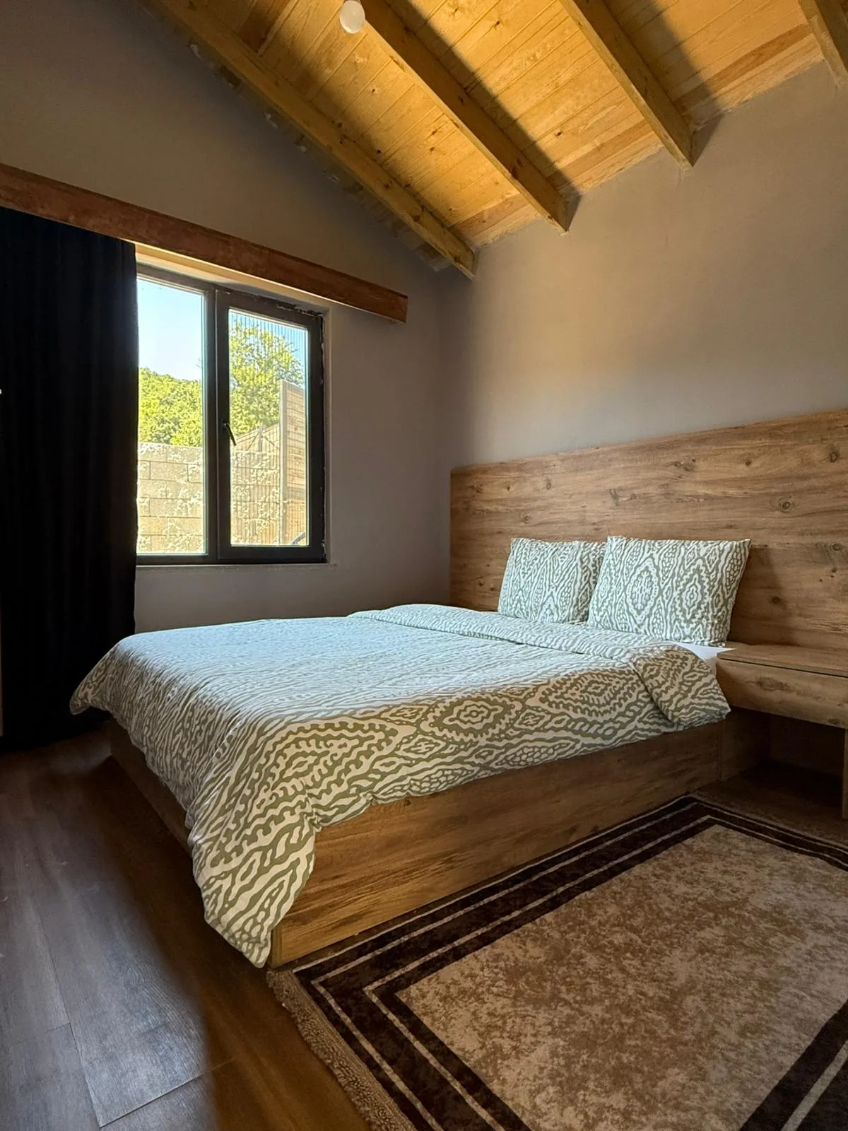 Platform yataklı ikinci yatak odası — doğal ahşap başlık ve orman manzaralı pencere